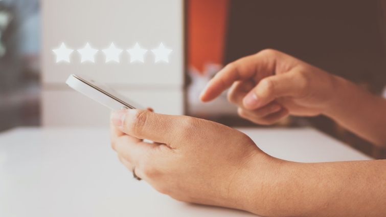 Small business owner pointing at a phone with five star review asking customer for referrals