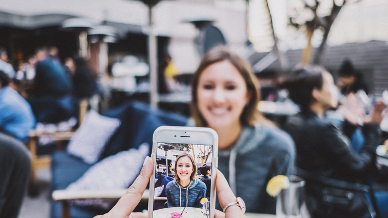 Person taking photo with smartphone of young woman smiling at restaurant