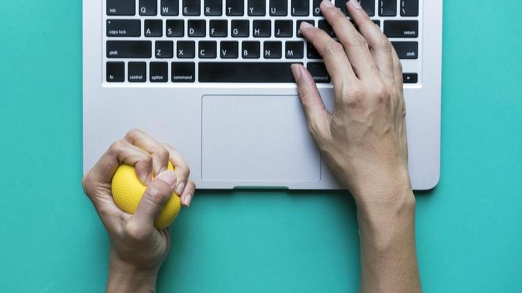 hand of a small business owner squeezing yellow stress ball in front of laptop