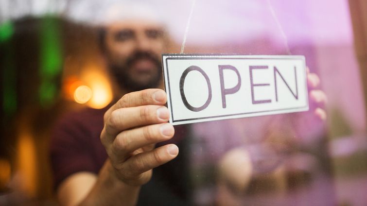 man putting an open sign on his small business because he received CARES Act funds