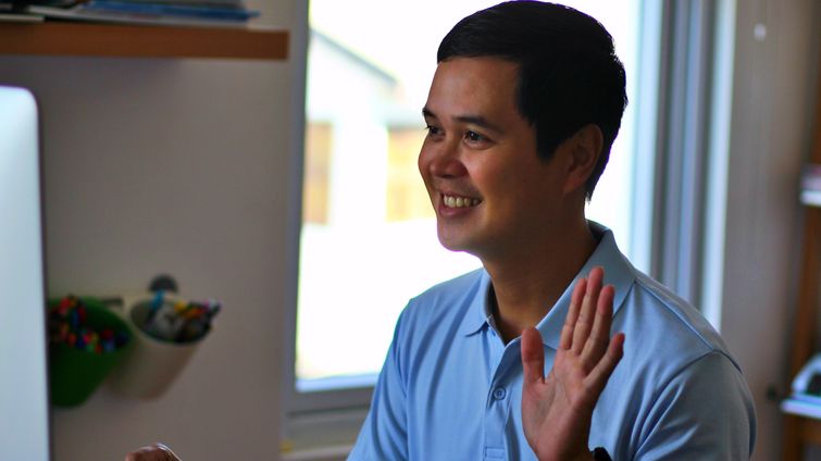 man waving at a computer screen at an online event