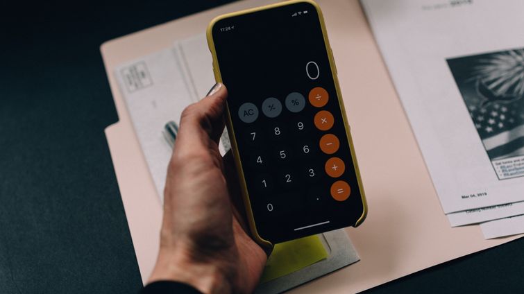 Woman holding calculator on phone displaying 0 with folders on desk