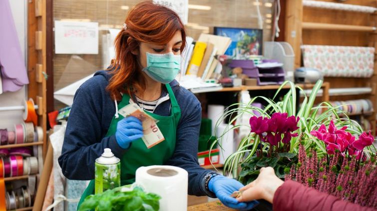 Small business owner in a mask giving change back to a customer at a floral shop