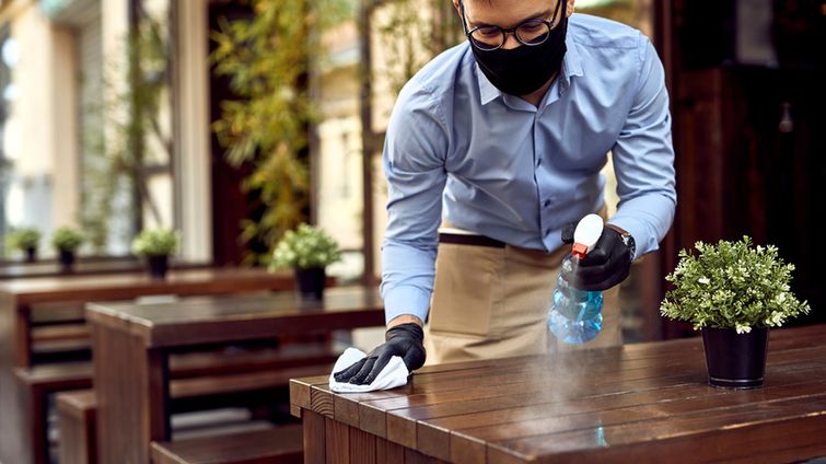 Man in mask at small business cleaning table outside showing small business resilience