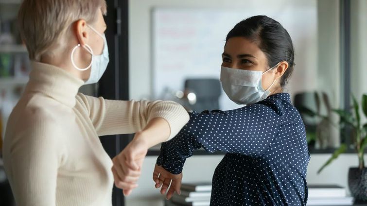 two female small business employees with masks bumping elbow