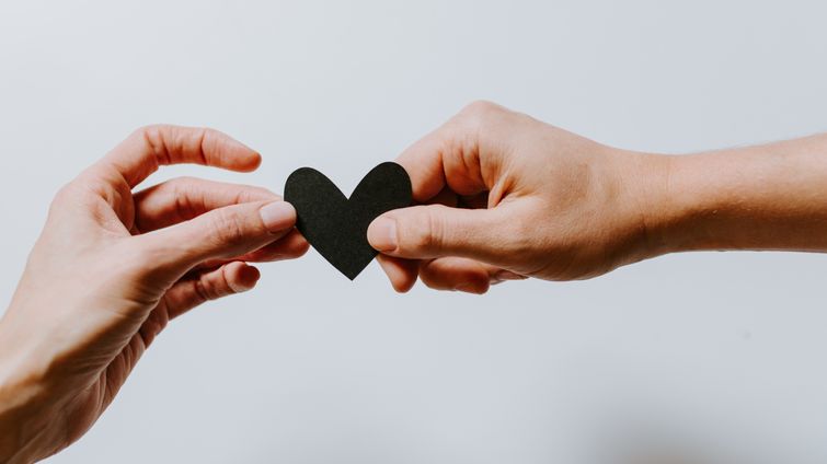 two hands holding a small black paper heart showing community support