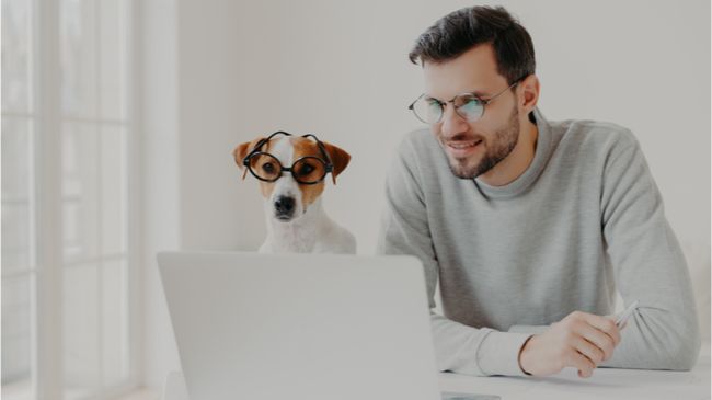 man in glasses looking at laptop screen with dog next to him