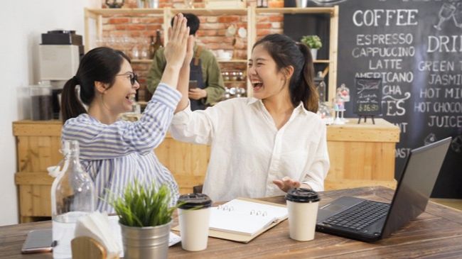 two women business owners celebrating and high fiving in cafe