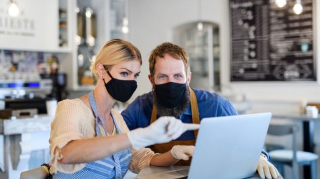 two business owners in masks pointing at laptop screen