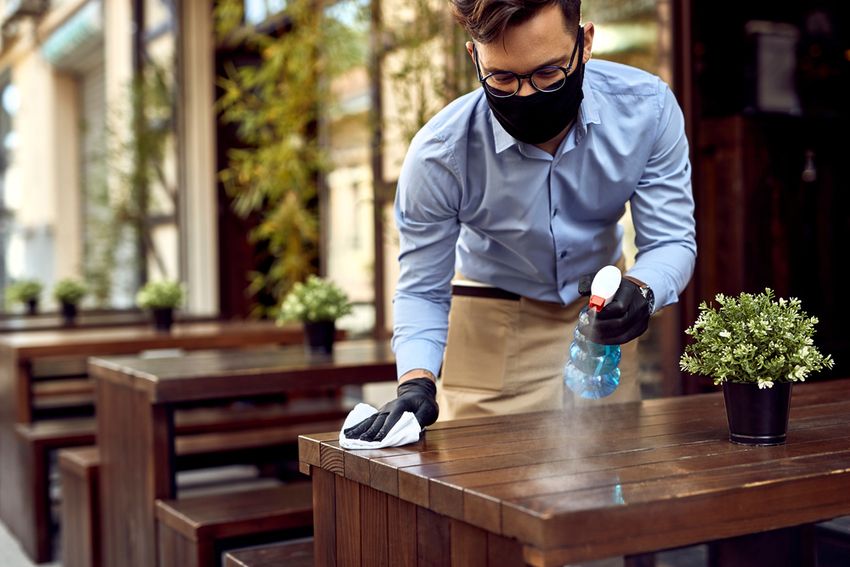 man in mask cleaning table at small business outside after coronavirus