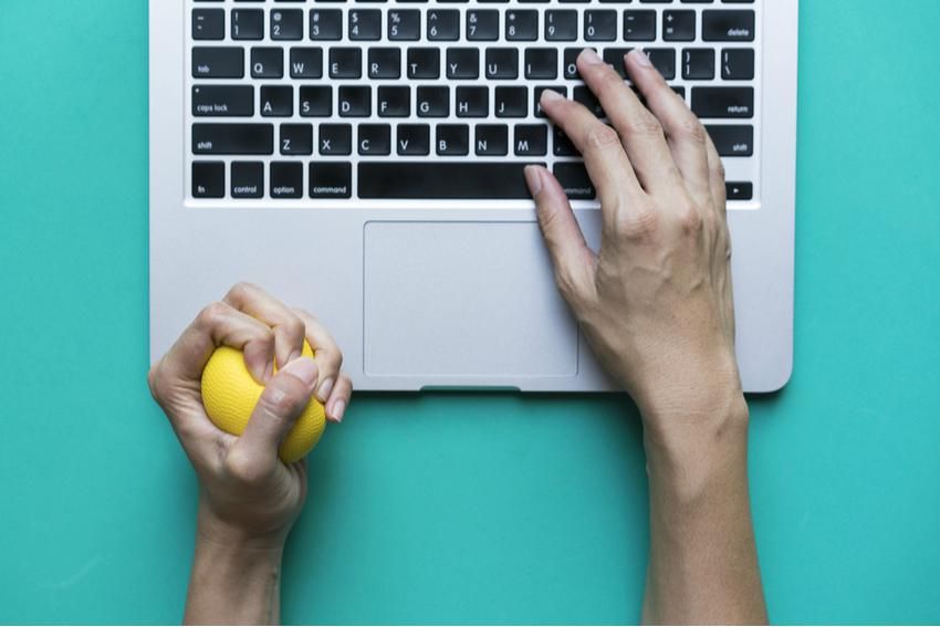 hand of a small business owner squeezing a yellow stress ball while typing on a laptop