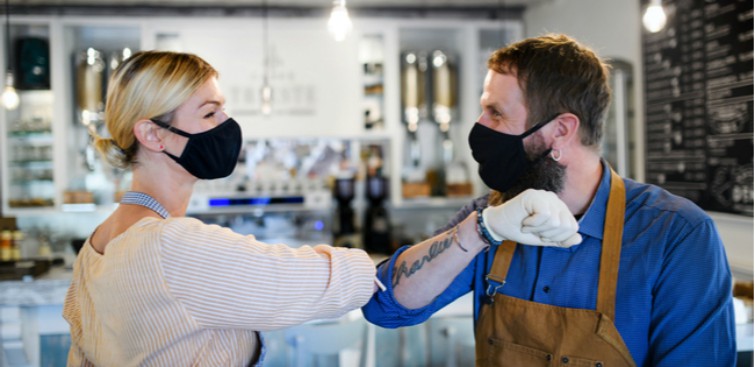 woman and man business owners wearing masks bumping elbows in store